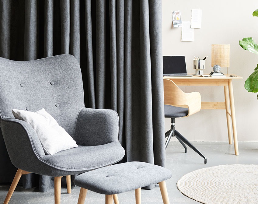 ANTEN curtains, HVIDOVRE office chair, VANDSTED desk and SKALBORG armchair with footstool Grey curtains separating a home office with desk and office chair from a living room with an armchair and footstool