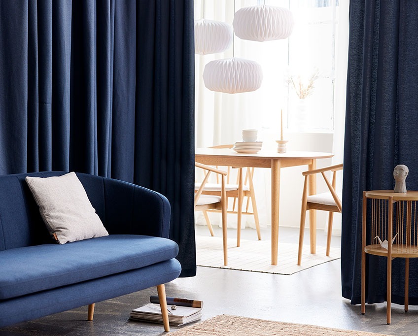 AMUNGEN curtain behind GISTRUP sofa and EGELEV end table with MARSTRAND dining table, ARNBORG dining chairs and VALDER lamps in the background Blue curtain behind a sofa separates a living area from a dining area
