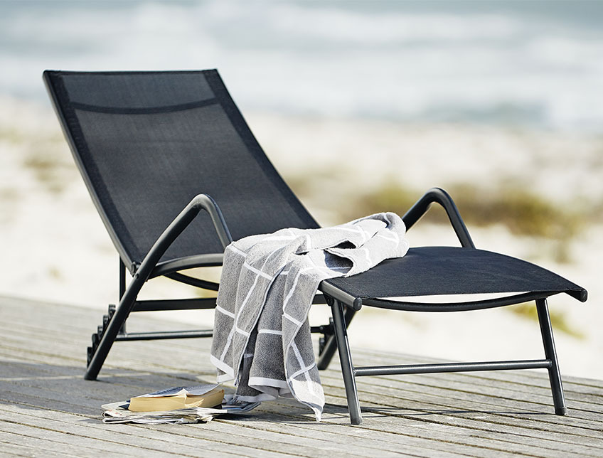 NORDSTRAND sun lounger Black sun lounger with armrests on a patio by the beach